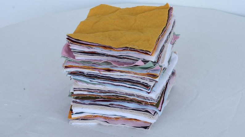 May include: A stack of fabric squares in various colors, including yellow, pink, green, and white. The squares are stacked neatly and are ready for a quilting project.
