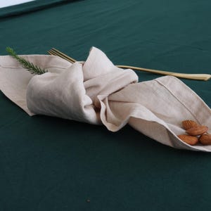 May include: A beige linen napkin folded and placed on a dark green tablecloth with a few almonds on top.