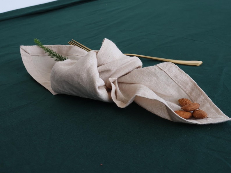 May include: A beige linen napkin folded and placed on a dark green tablecloth with a few almonds on top.