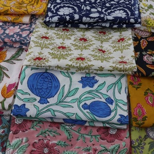 Op de afbeelding: Een verzameling kleurrijke stofstalen met bloemenpatronen. De stoffen zijn gevouwen en op elkaar gestapeld, waardoor een verscheidenheid aan texturen en kleuren ontstaat.