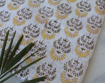 May include: White cotton fabric with a repeating pattern of yellow and green floral designs. The fabric is folded and a green leaf is lying on top of it.