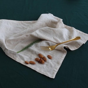 May include: A white linen napkin with a gold fork and almonds on a dark green surface.