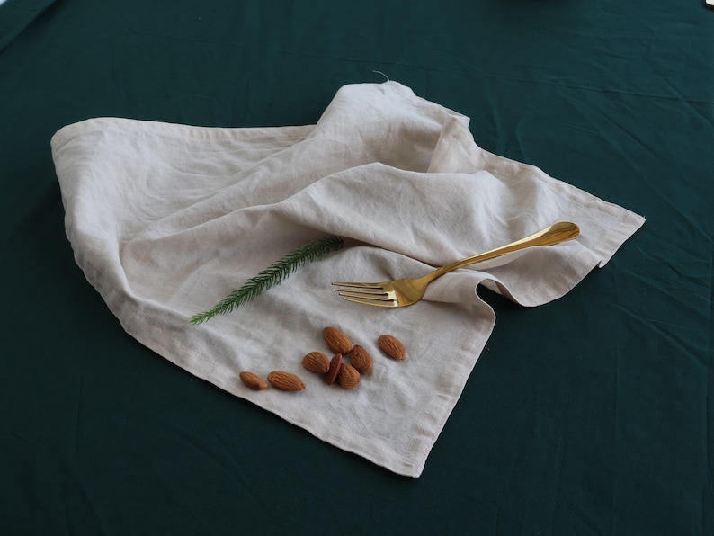 May include: A white linen napkin with a gold fork and almonds on a dark green surface.
