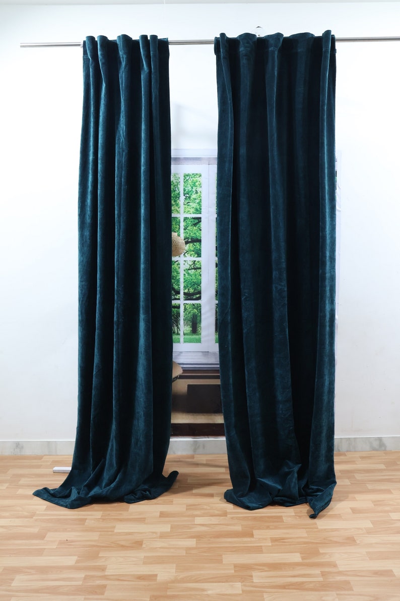 May include: Two teal velvet curtains hanging from a curtain pole in front of a window. The curtains are fully extended and reach the floor.