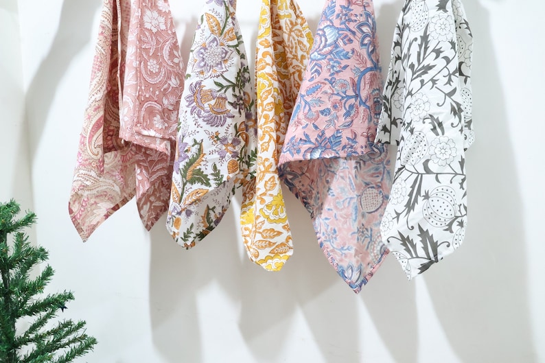 Puede incluir: Seis toallas de cocina con diferentes patrones colgadas en una pared blanca. Las toallas son de algod&oacute;n y presentan dise&ntilde;os florales en tonos rosa, azul, amarillo y blanco.