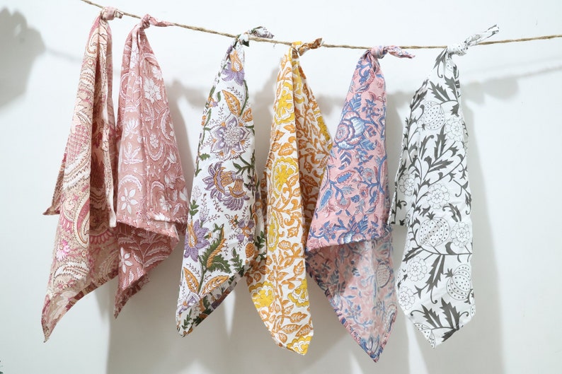 Puede incluir: Cinco toallas de t&eacute; de algod&oacute;n con patrones florales en varios colores, incluyendo rosa, amarillo, blanco y negro. Las toallas est&aacute;n colgadas de una cuerda.