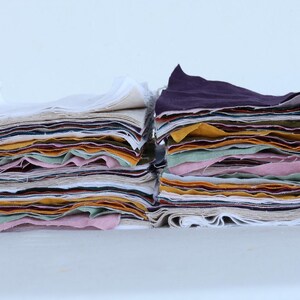 May include: Two stacks of fabric squares in various colors, including white, pink, yellow, green, and brown. The fabric squares are layered on top of each other, creating a colorful and textured display.