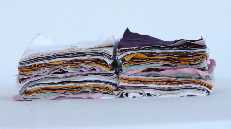 May include: Two stacks of fabric squares in various colors, including white, pink, yellow, green, and brown. The fabric squares are layered on top of each other, creating a colorful and textured display.