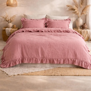 May include: A dusty rose-colored bed set with ruffled edges. The set includes a duvet cover and two pillow shams. The bedding is on a bed with a neutral-colored rug and a woven pendant light.