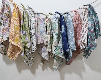 May include: A collection of ten colourful fabric squares with floral patterns, hanging on a white wall. The squares are tied together with string.
