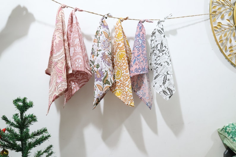 Puede incluir: Seis cuadrados de tela coloridos con patrones florales est&aacute;n colgados en un tendedero. Los cuadrados son en tonos de rosa, morado, amarillo y negro.