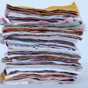 May include: A stack of fabric scraps in various colors, including white, pink, yellow, brown, and blue. The fabric is layered and folded, creating a textured and colorful display.