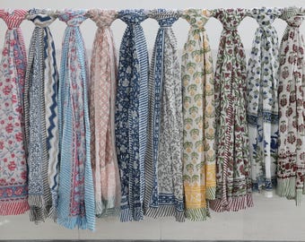 May include: A collection of ten printed cotton scarves in various colors and patterns, including floral, geometric, and paisley designs. The scarves are hanging on a white rod.