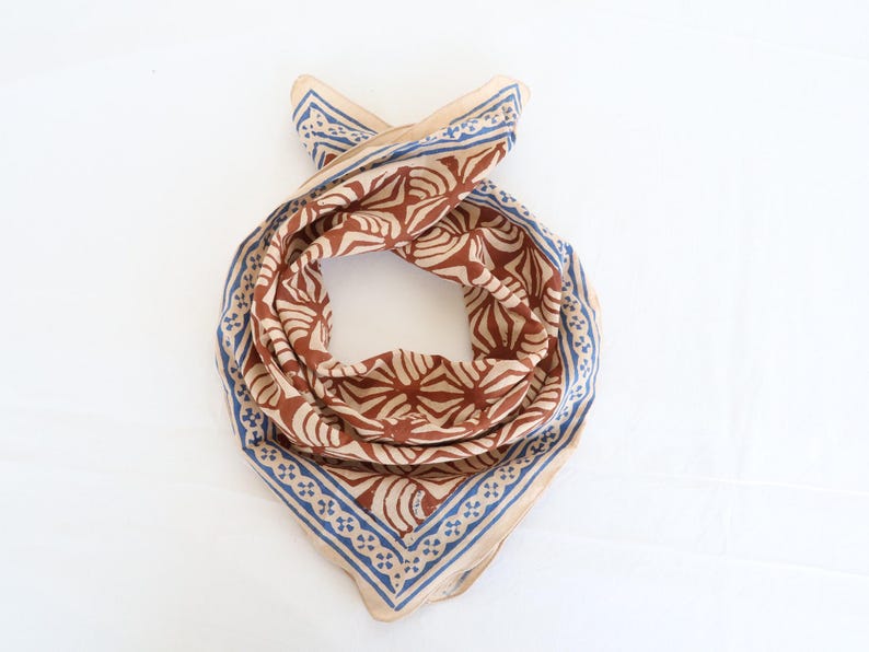 Może przedstawiać: Brązowo-beżowa bandana z kwiatowym wzorem i niebieskim obramowaniem. Bandana jest złożona w kształt tr&oacute;jkąta.