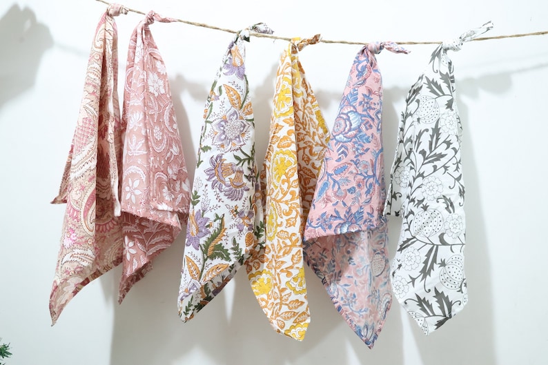 Puede incluir: Cinco toallas de t&eacute; de algod&oacute;n con patrones florales en varios colores, incluyendo rosa, morado, amarillo, azul y blanco. Las toallas est&aacute;n colgadas en un tendedero.