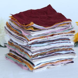 May include: A stack of fabric squares in various colors and patterns, including red, yellow, white, and blue. The fabric squares are neatly stacked and ready for a quilting project.
