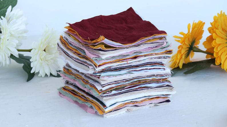 May include: A stack of fabric squares in various colors and patterns, including red, yellow, white, and blue. The fabric squares are neatly stacked and ready for a quilting project.