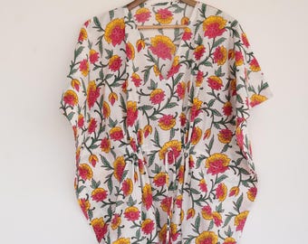 May include: White cotton kaftan with a floral print in shades of pink, yellow, and green. The kaftan has a V-neck and short sleeves. It has a drawstring at the waist.