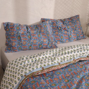 Peut inclure: Ensemble de literie avec des taies d'oreiller et une courtepointe à motifs floraux bleus. Les taies d'oreiller présentent des motifs floraux orange et verts sur fond bleu. La courtepointe a un design similaire avec une bordure blanche.