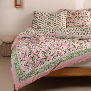 Può includere: Un set di biancheria da letto floreale con un motivo floreale rosa e verde su sfondo bianco. Il set include una trapunta e due federe abbinate. La trapunta ha un bordo rosa con un motivo floreale verde e bianco.