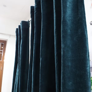 May include: A set of dark teal velvet curtains hanging from a curtain pole. The curtains are lined up in a row and are all the same length.