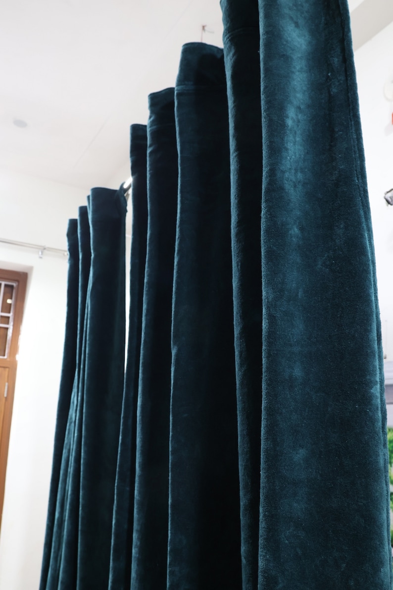 May include: A set of dark teal velvet curtains hanging from a curtain pole. The curtains are lined up in a row and are all the same length.