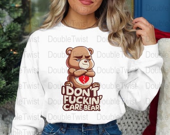 May include: White sweatshirt with a graphic of a brown bear with a broken heart. The text "I DON'T FUCKIN' CARE BEAR" is printed below the bear.