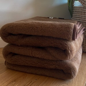 May include: A brown wool blanket folded in thirds. The blanket is soft and fluffy, and it would be perfect for keeping warm on a cold day.