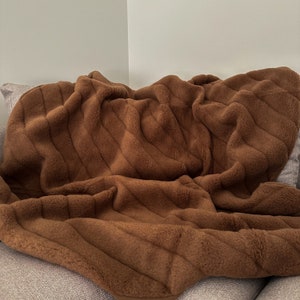 May include: A brown plush throw blanket with a quilted pattern. The blanket is folded and draped over a couch.