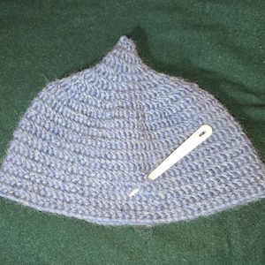 Puede incluir: Un gorro de punto gris con la parte superior puntiaguda. Una aguja de plástico blanca sobresale del gorro.