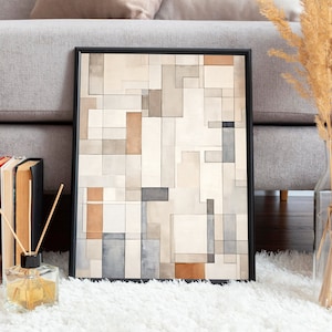 May include: A framed abstract geometric print with a black frame, featuring a pattern of beige, brown, and gray squares and rectangles. The print is sitting on a white fluffy rug in front of a gray sofa.