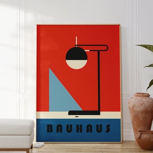 Könnte beinhalten: Ein rotes, blaues und weißes Poster mit einem geometrischen Lampendesign in Schwarzweiß. Das Poster trägt den Schriftzug "BAUHAUS" in schwarzen Buchstaben auf blauem Hintergrund.