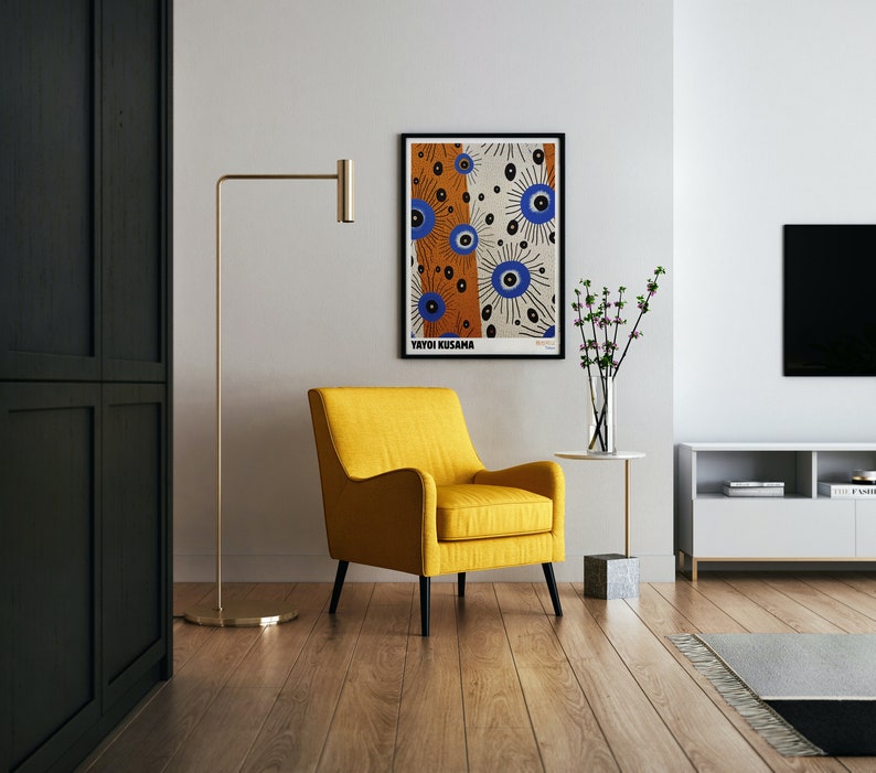 May include: A yellow armchair with black legs sits in a living room with a black floor lamp, a white wall, and a framed poster with the text "Yayoi Kusama" and a colorful abstract design.