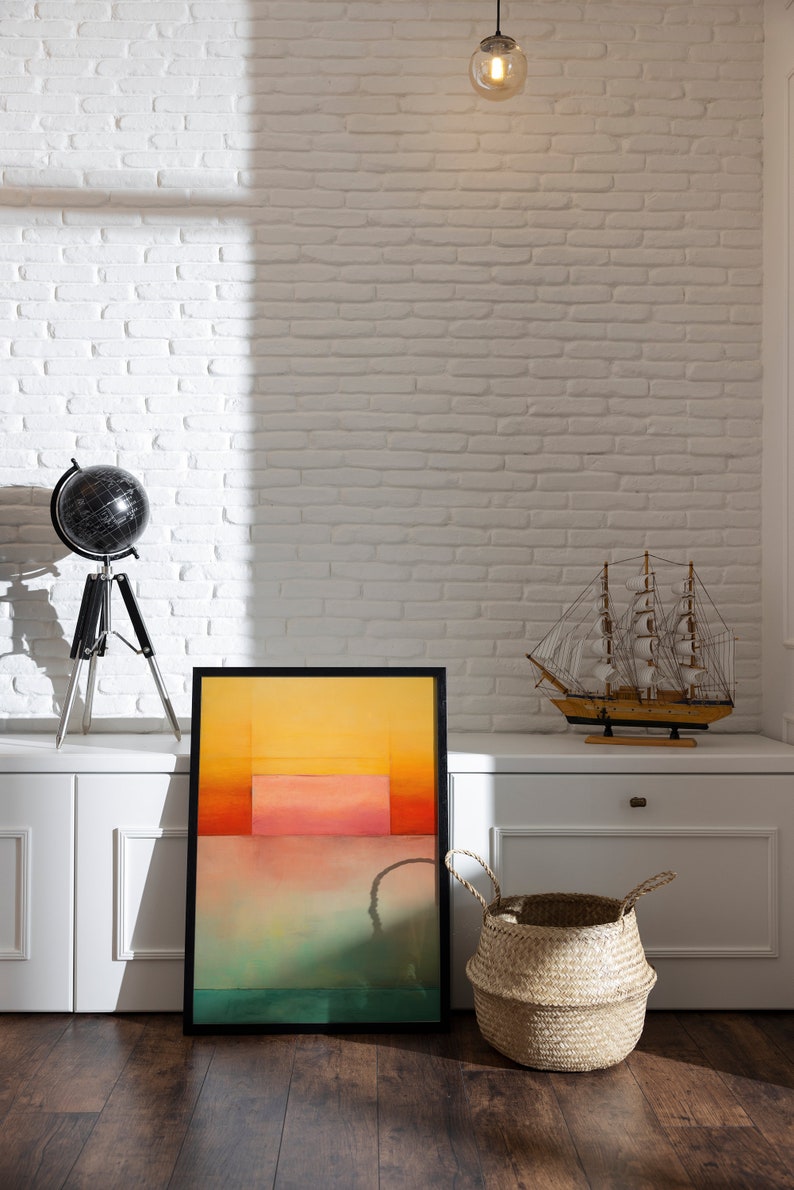 Peut inclure: Une peinture abstraite encadr&eacute;e aux couleurs jaune, orange, rose et verte est accroch&eacute;e &agrave; un mur en briques blanches au-dessus d'une armoire blanche. Un globe terrestre sur un tr&eacute;pied se trouve sur l'armoire &agrave; gauche de la peinture. Un petit voilier en bois se trouve sur l'armoire &agrave; droite de la peinture. Un panier en osier se trouve sur le sol devant l'armoire.