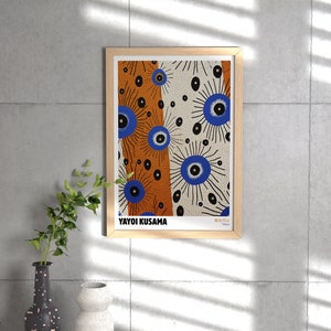 May include: A framed print of a colorful abstract art piece by Yayoi Kusama. The artwork features a pattern of blue eyes with black outlines and white and orange backgrounds. The print is titled "Beautiful" and is signed "Yayoi Kusama, Tokyo."