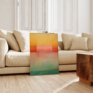 Peut inclure: Impression d'art abstrait avec un sch&eacute;ma de couleurs jaune, orange, rose, bleu et vert. L'impression est encadr&eacute;e dans un cadre dor&eacute; et est appuy&eacute;e contre un canap&eacute; beige.