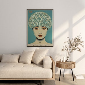 May include: A framed art print depicting a woman with a polka-dot head covering against a teal backdrop. The print includes the name "YAYOI KUSAMA". The artwork is displayed above a beige sofa in a living room setting.