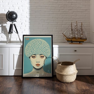 May include: Framed art print depicting a woman with a polka-dot head covering. The artwork has a teal background and the name "YAYOI KUSAMA" is printed at the bottom. The print is displayed on a wooden floor.