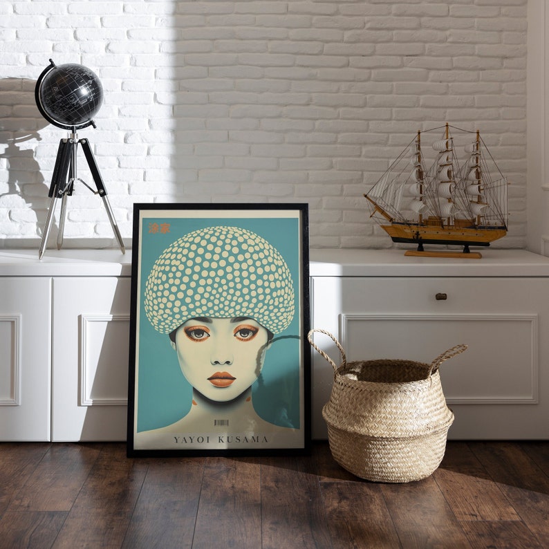 May include: Framed art print depicting a woman with a polka-dot head covering. The artwork has a teal background and the name "YAYOI KUSAMA" is printed at the bottom. The print is displayed on a wooden floor.