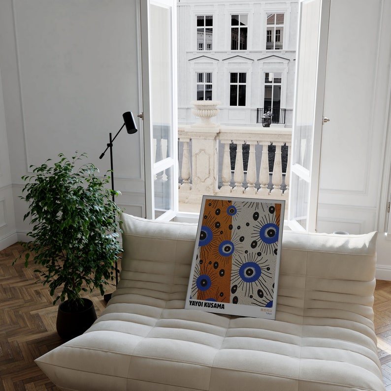 May include: A white couch with a framed print of a colorful abstract design featuring blue and orange circles. The print is titled "Yayoi Kusama".