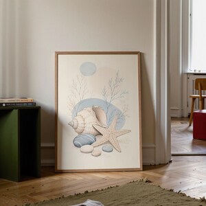 Könnte beinhalten: Ein gerahmter Kunstdruck mit beigem Hintergrund und einer zentralen Illustration einer großen Spiralschnecke, einem fünfzackigen Seestern und mehreren glatten Kieselsteinen, ergänzt durch zarte blaue Linienzweige und weiche Kreise.