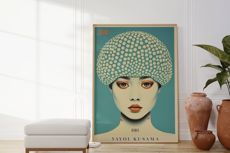 May include: A framed art print depicting a woman with a dotted head covering and orange makeup. The artwork has a teal background and the name "Yayoi Kusama" is printed at the bottom. The frame is a light wood colour.
