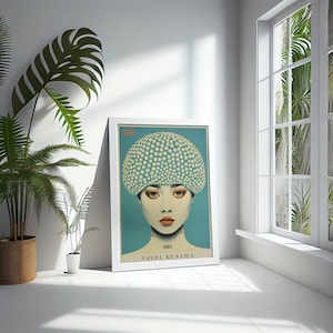 May include: A framed art print depicting a woman with a polka-dot head covering. The artwork has a teal background and the name "YAYOI KUSAMA" is printed at the bottom. The print is in a white frame, leaning against a white wall.