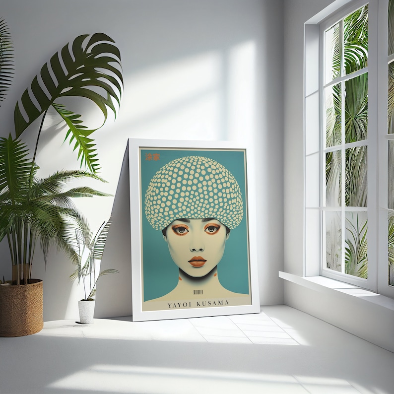May include: A framed art print depicting a woman with a polka-dot head covering. The artwork has a teal background and the name "YAYOI KUSAMA" is printed at the bottom. The print is in a white frame, leaning against a white wall.