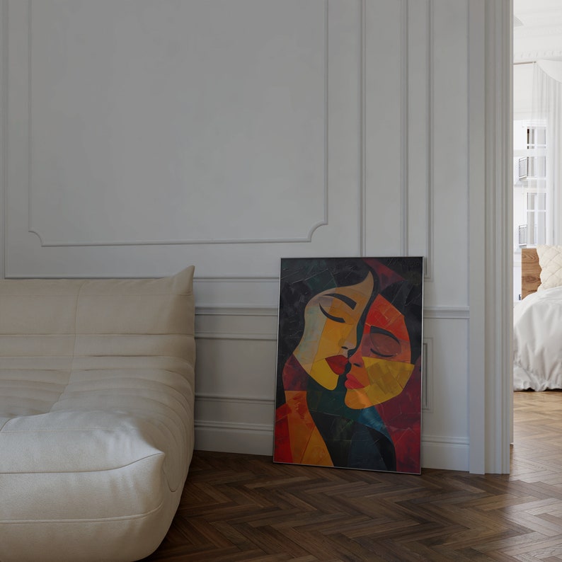 May include: Abstract painting of two faces in a close embrace, with a colourful palette of red, yellow, orange, and blue. The painting is framed in a black frame and is hanging on a white wall.