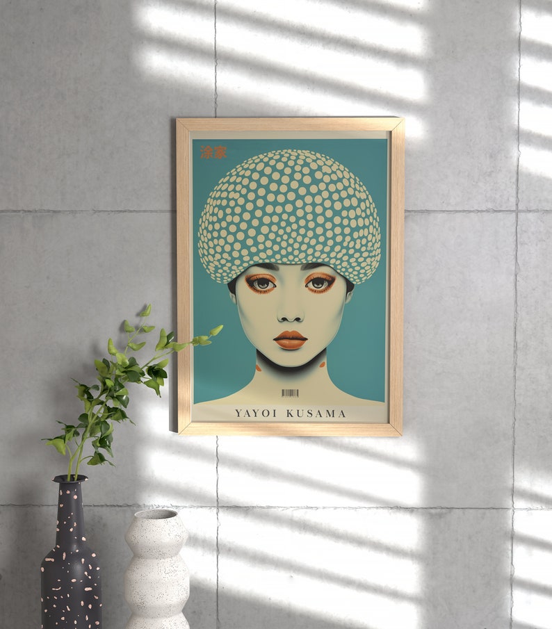 May include: A framed art print of a woman with a dotted head covering and orange makeup. The artwork, set against a teal background, is signed "YAYOI KUSAMA" and is in a light wood frame. The image is displayed on a concrete wall.