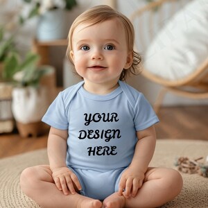 May include: A baby wearing a light blue onesie with the text "YOUR DESIGN HERE" in black. The baby is sitting on a round, woven rug. The background includes plants and a wooden chair.