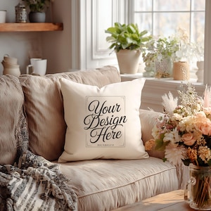 May include: Cream-colored square pillow with the text "Your Design Here" in a black, elegant script. The pillow is on a beige corduroy sofa, with a floral arrangement and a window in the background. The pillow is a home decor item.