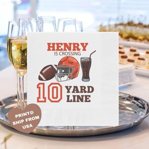 May include: White square paper napkins with a football theme. The design includes a football, helmet, and a glass of soda. Text reads "HENRY IS CROSSING 10 YARD LINE". A heart-shaped sticker says "PRINT & SHIP FROM USA".