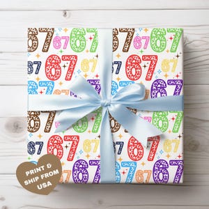 May include: A wrapped gift with a light blue satin ribbon. The wrapping paper features a repeating pattern of the numbers 6 and 7 in various colors and animal print textures, with star accents. The text "PRINT & SHIP FROM USA" is on a heart-shaped tag.